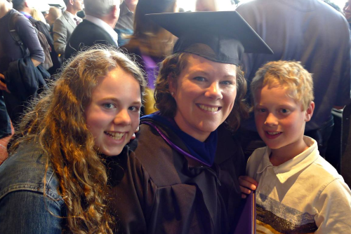 Dana wearing a graduation cap and gown next to her children