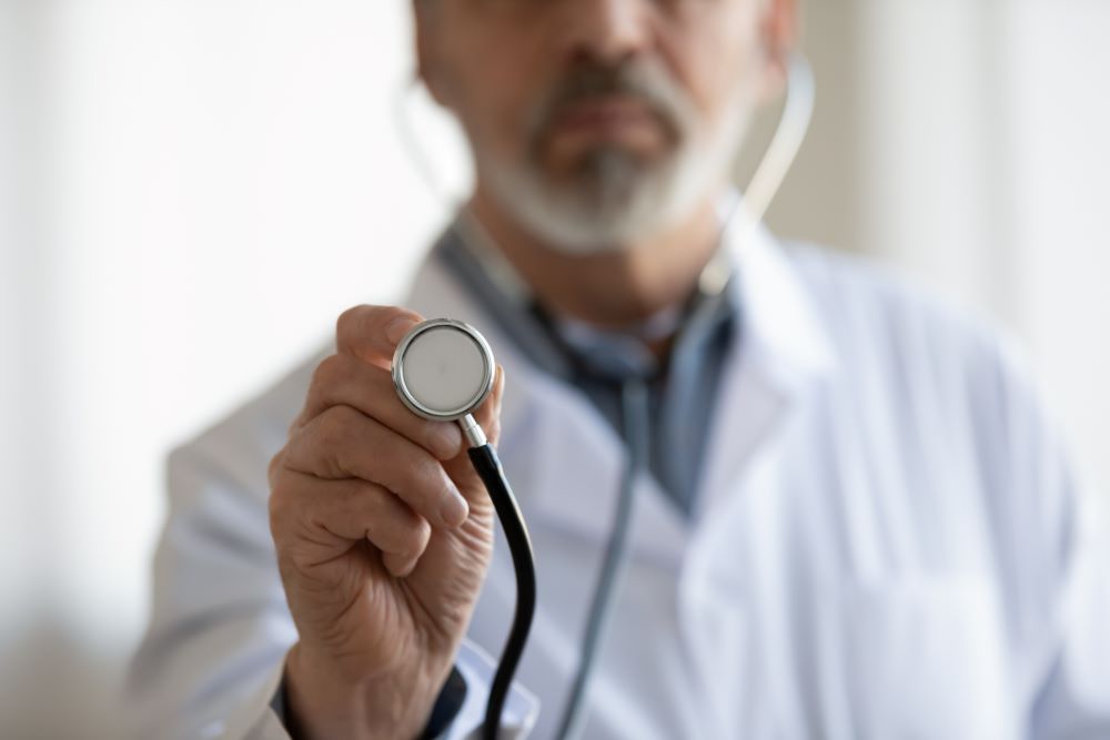Crop close up of mature male doctor in white medical uniform hold stethoscope
