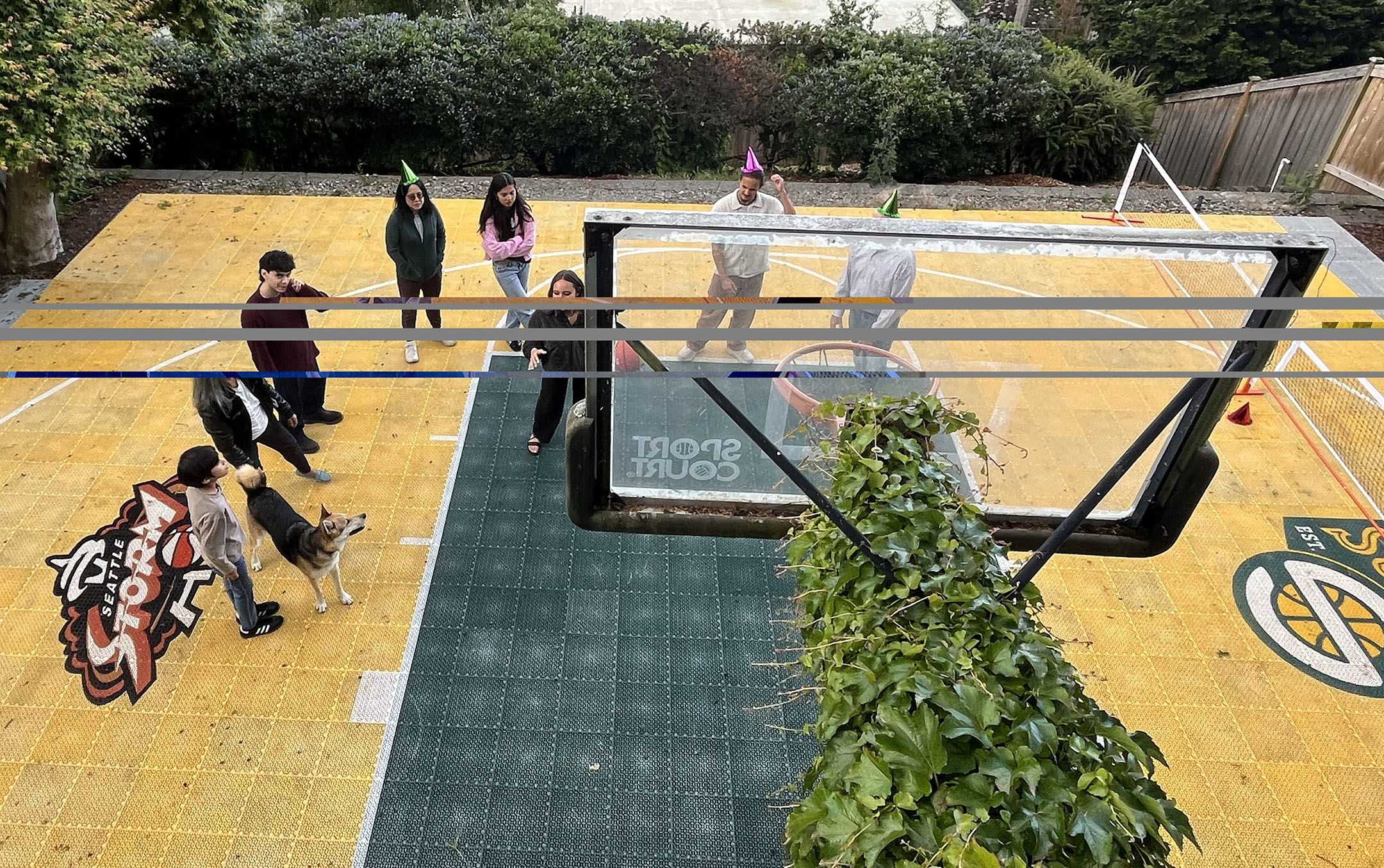 Backyard basketball court with people standing around in birthday hats